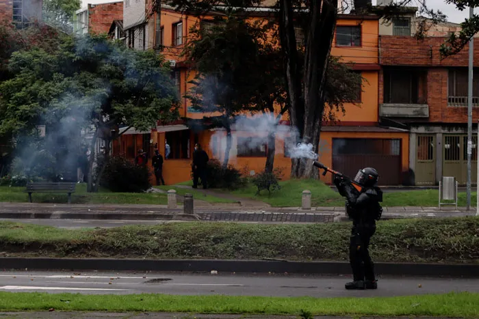 Agente antidisturbios dispara gas lacrimógeno en una calle con edificios de ladrillo al fondo