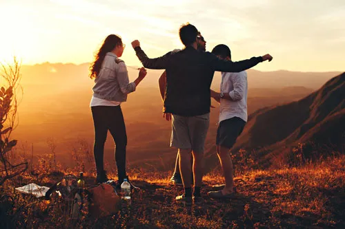 Tres amigos de espaldas con los brazos abiertos frente a montañas al atardecer