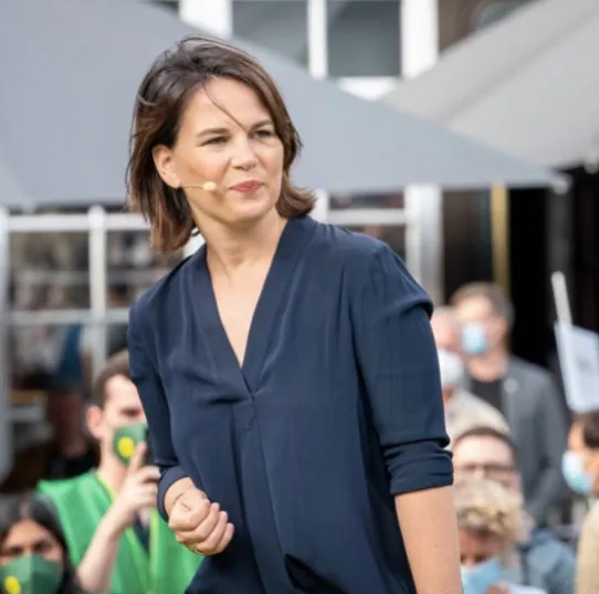 Annalena Baerbock, con micrófono de diadema y blusa azul oscuro, habla ante un público con mascarillas en un acto al aire libre