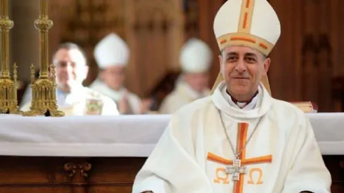 Arzobispo con mitra y vestiduras blancas sonríe sentado ante un altar junto a otros obispos