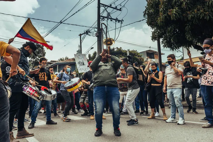 Banda callejera con tambores y trombón entre manifestantes y banderas de Colombia