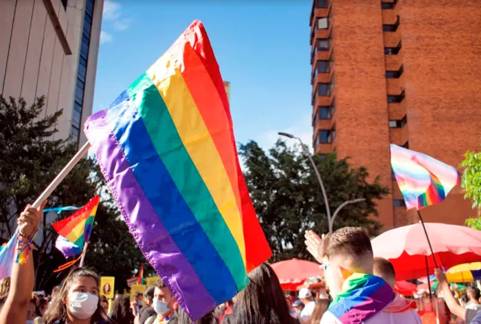 Bandera arcoíris ondeando entre asistentes con mascarilla a una marcha del orgullo LGBT+