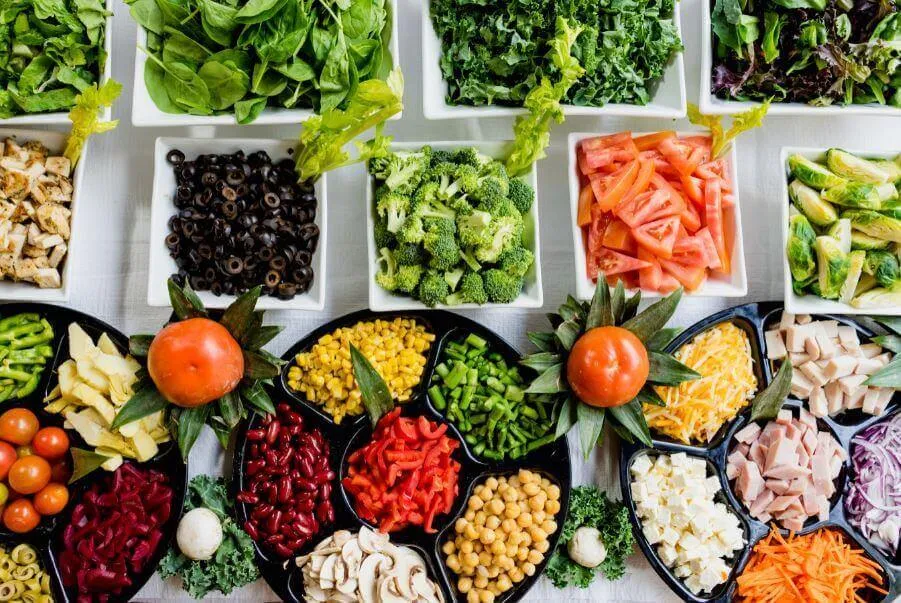 Vista aérea de una barra de ensaladas con recipientes de verduras, legumbres y frutas de colores
