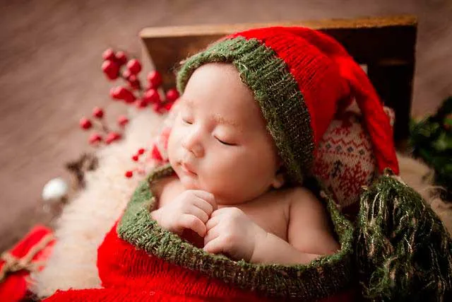 Bebé dormido con gorro de lana verde y rojo entre adornos navideños