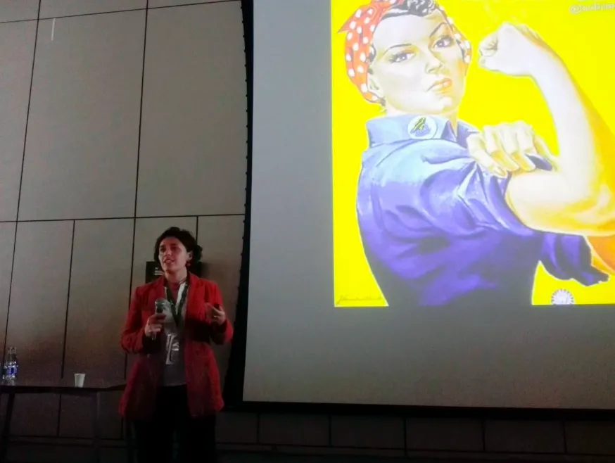 Bibian Rojas, ecóloga, con chaqueta roja, expone ante una diapositiva con la imagen de «Rosie la remachadora»