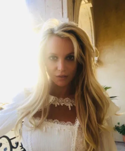 Britney Spears, mujer de cabello largo y rubio con blusa blanca de encaje, mira a la cámara en un retrato