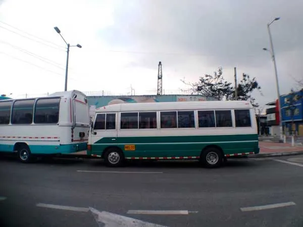 Dos buses blancos y verdes circulan por una avenida de Bogotá bajo un cielo nublado