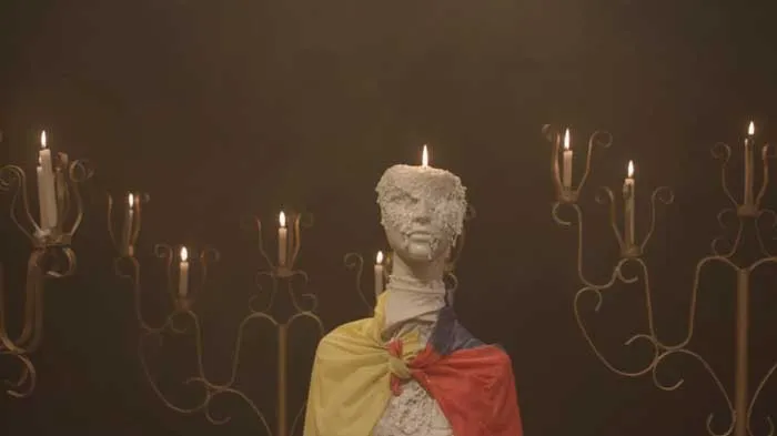 Busto de cera con una vela encendida, envuelto en la bandera de Colombia entre candelabros