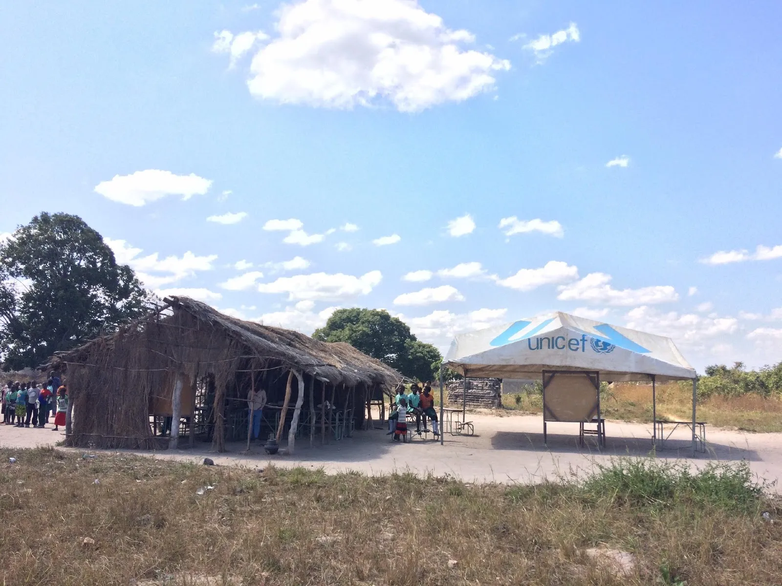 Cabaña de paja y una carpa de UNICEF en un descampado bajo un cielo con nubes