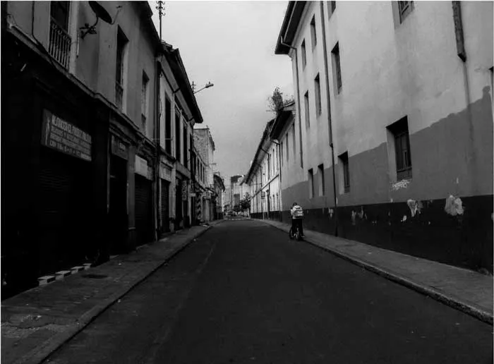 Calle estrecha del barrio Santa Fe en Bogotá flanqueada por fachadas antiguas, en blanco y negro