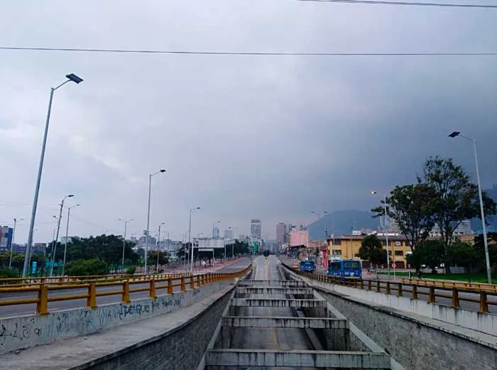 Canal de concreto que atraviesa una avenida de Bogotá bajo un cielo gris, sin tráfico