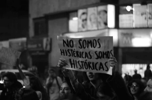 Manifestante sostiene un cartel con la frase «No somos histéricas, somos históricas» en una marcha nocturna, en blanco y negro