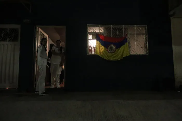 Fachada oscura de una casa con personas en la puerta y una bandera de Colombia colgada en la ventana