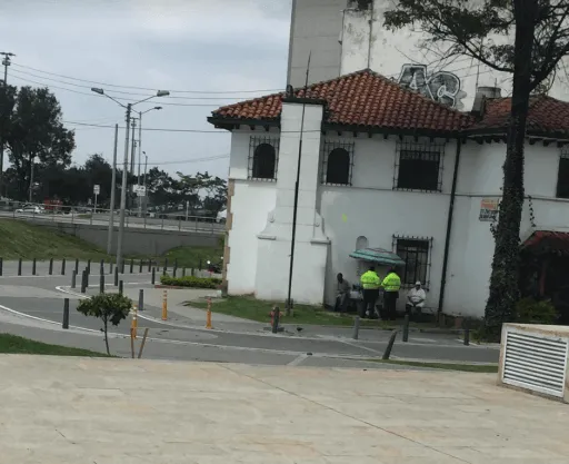 Casa blanca de techo de tejas junto a una calle, con dos agentes con chaleco amarillo frente a la puerta