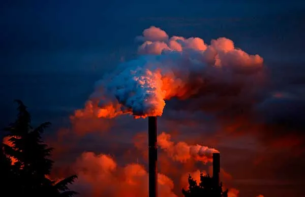 Chimenea industrial que expulsa humo espeso entre nubes rojizas al atardecer