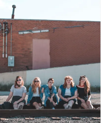 Cinco jóvenes con gafas de sol sentadas juntas frente a un muro de ladrillo