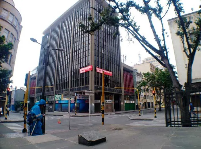 Edificio de oficinas y calle casi desierta en Bogotá, con una persona con traje de bioseguridad al fondo