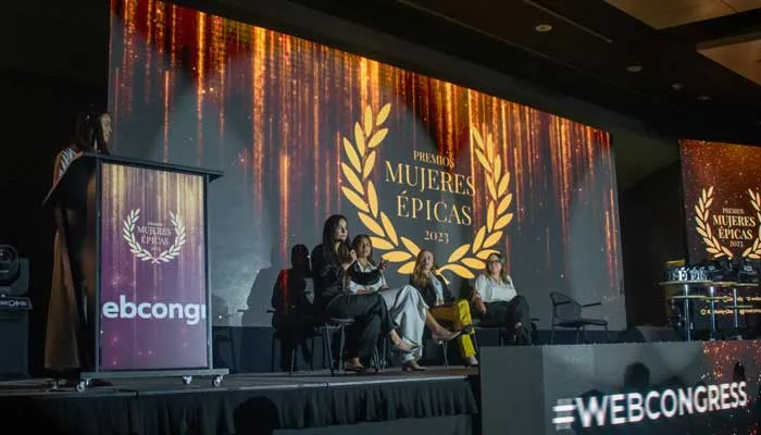 Escenario de la gala Mujeres Épicas 2023 con un panel de mujeres, un atril y el logo de laurel en la pantalla