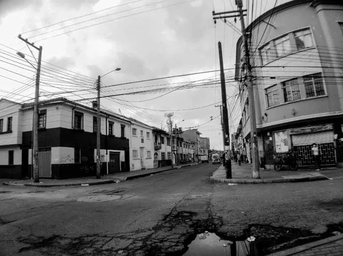 Esquina del barrio Santa Fe en Bogotá con cables de luz y un charco en la calle, en blanco y negro