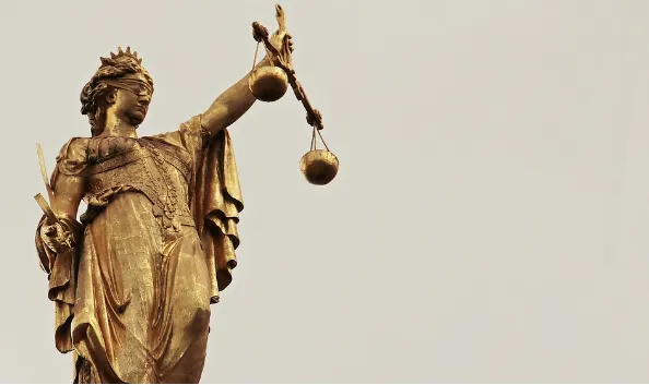 Estatua dorada de la Justicia sosteniendo una balanza sobre un fondo beige