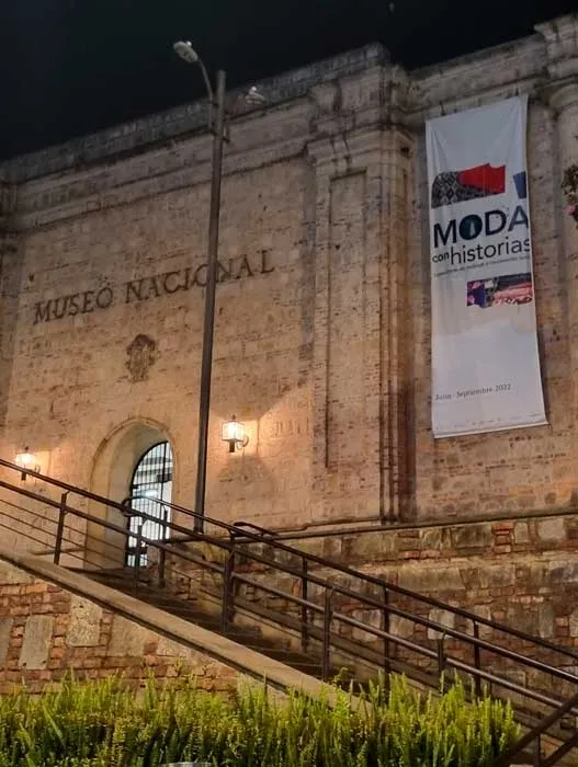 Fachada nocturna del Museo Nacional con un pendón de la exposición «Moda con historias»