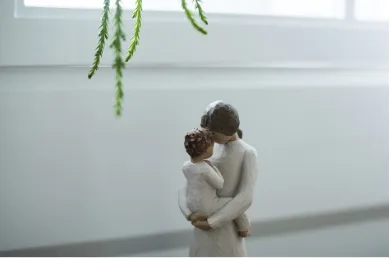 Figura de porcelana de una madre abrazando a su hijo, con ramas verdes colgando sobre ellos