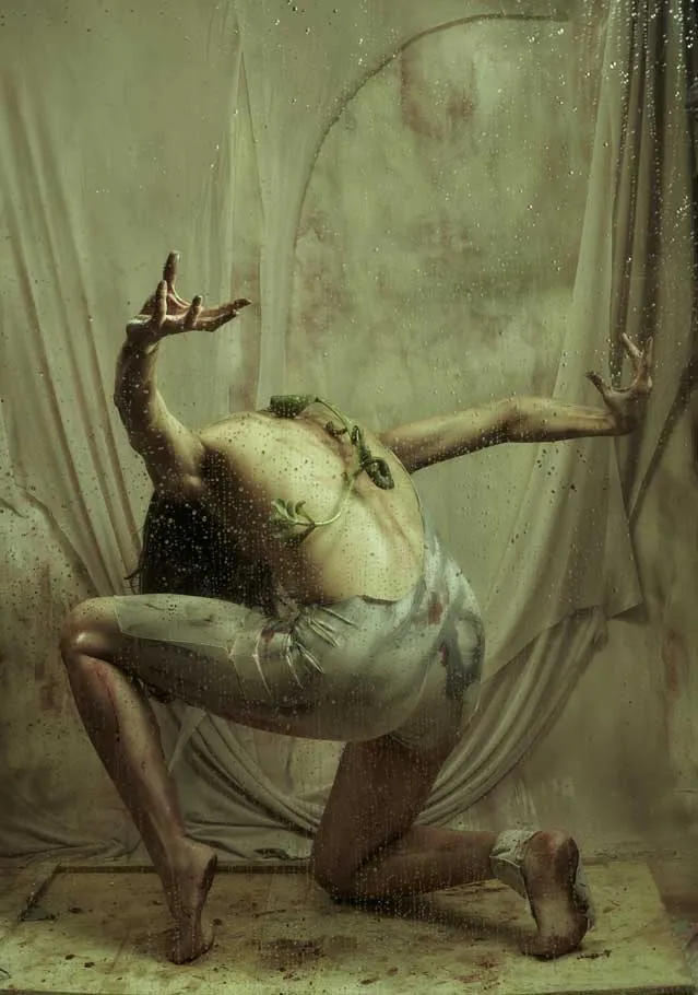 Bailarina arrodillada de espaldas con los brazos extendidos ante una tela vieja, en una foto-performance sobre el feminicidio