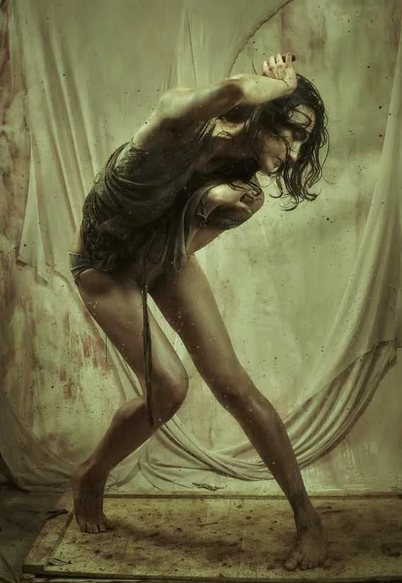 Bailarina de pie con el cuerpo inclinado y los brazos cruzados sobre el rostro ante una tela vieja, en una foto-performance sobre el feminicidio