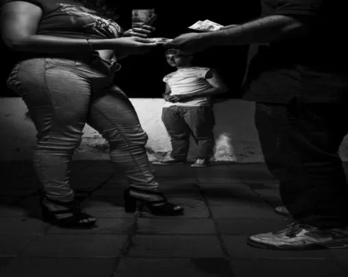 Piernas de varias personas en una calle de noche, una mujer con tacones recibe dinero, de la serie «Una oportunidad se convirtió en la peor pesadilla»