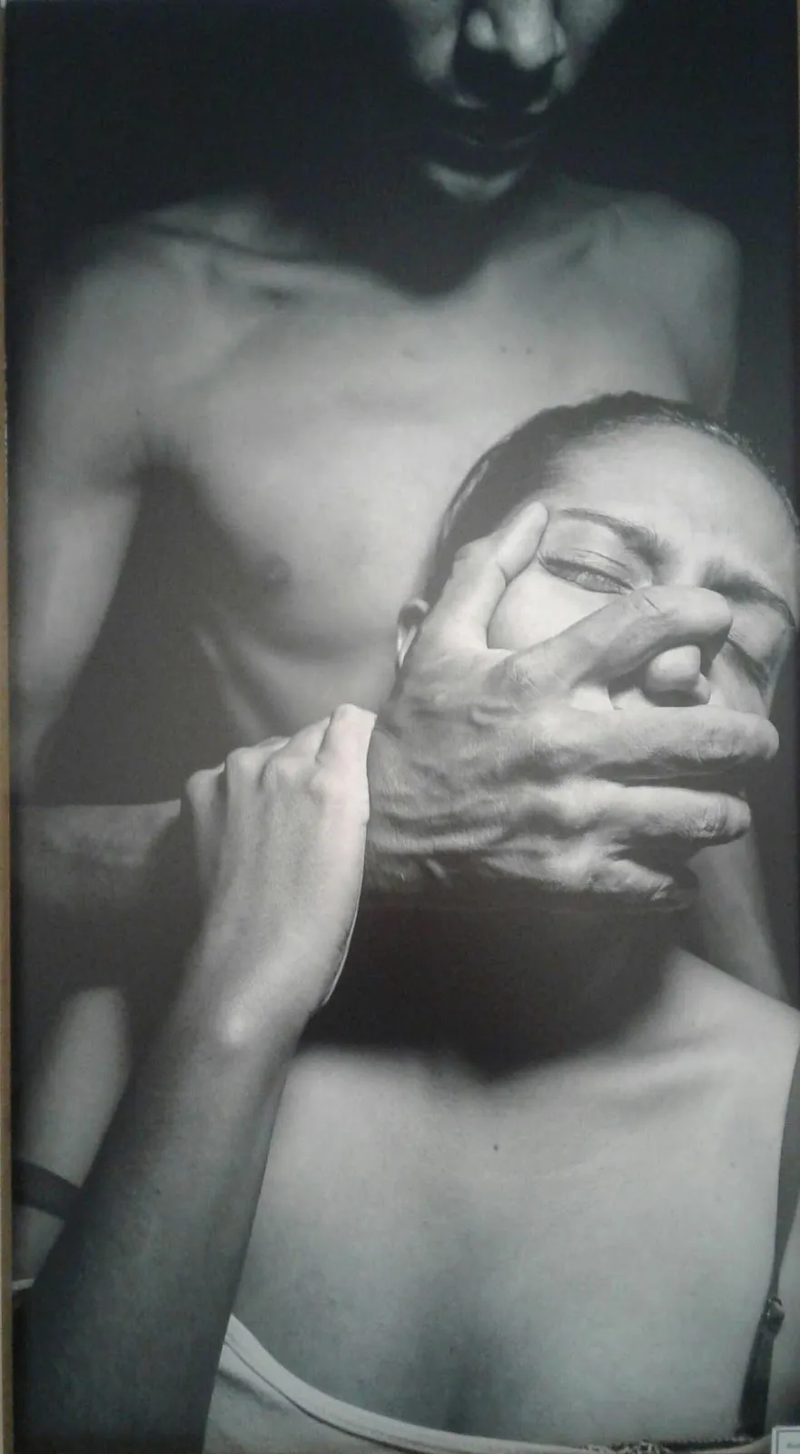 Hombre sin camisa cubre con la mano la boca de una mujer, imagen en blanco y negro de la serie «Tuve que callar por años»