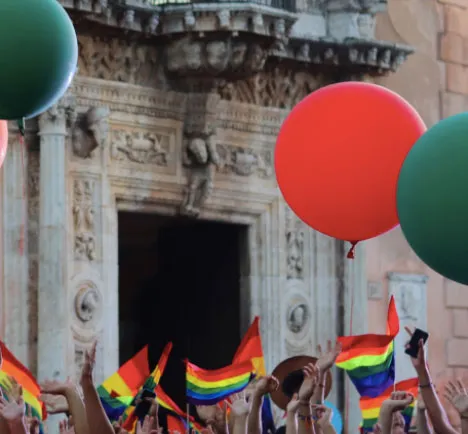 Globos rojos y verdes y banderas del arcoíris frente a un edificio de fachada de piedra
