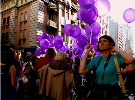 Globos morados en una calle de Montevideo y una mujer con cámara al cuello durante una marcha