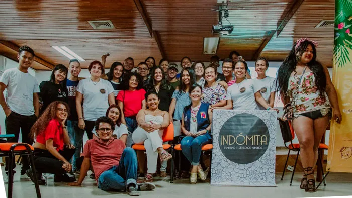 Grupo numeroso de personas posa en un salón junto a una pancarta que dice «Indómita»