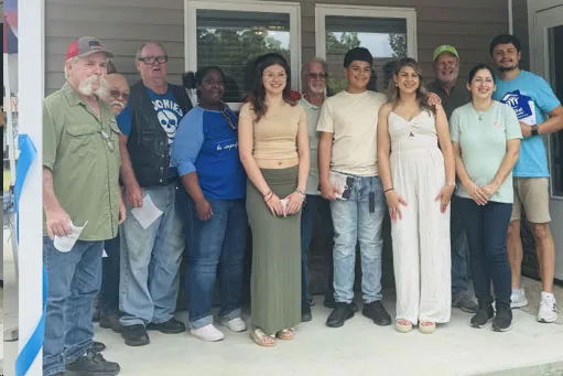 Grupo de voluntarios y familias posan en el porche de una casa nueva