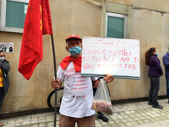 Hombre con tapabocas y bandera roja sostiene un cartel contra el gobierno en una acera del Paro Nacional