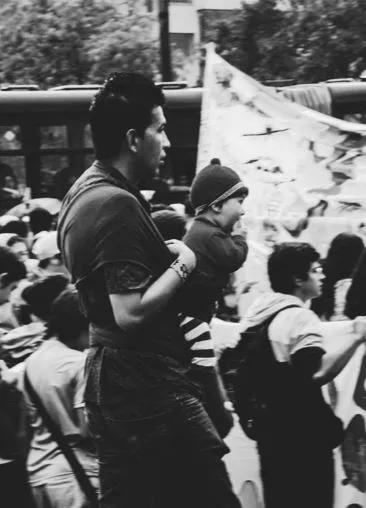 Hombre carga a un niño con gorro entre una multitud en una marcha, en blanco y negro
