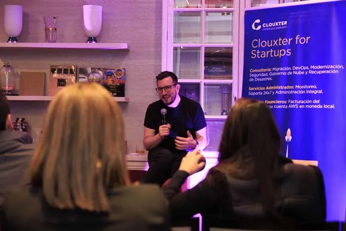 Hombre con micrófono en una charla junto a un pendón «Clouxter for Startups», con público en primer plano