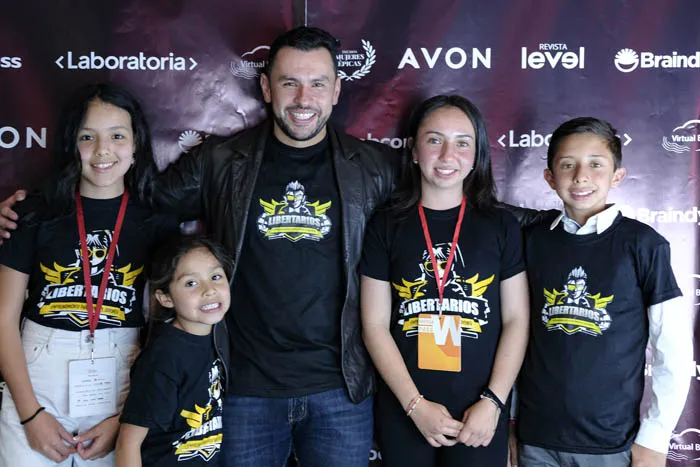 Un hombre y tres niñas con camisetas iguales posan frente al panel de Revista Level, Avon y Braindy