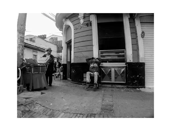 Hombres sentados y de pie en la esquina de un edificio antiguo en la ciudad, en blanco y negro