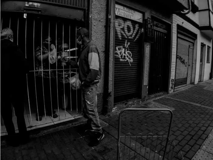 Dos hombres frente a un local con reja cerrada y grafitis en el centro de Bogotá durante la cuarentena