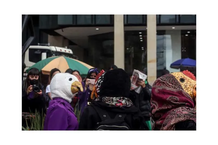 Manifestantes con máscaras de ave, pañuelos y sombrillas frente a un edificio durante el 8 de marzo
