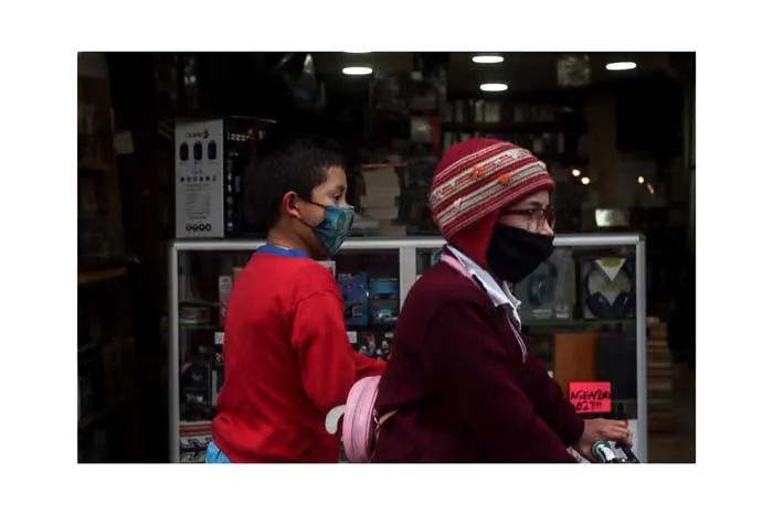 Mujer con gorro rojo y mascarilla y un niño con sudadera roja caminan frente a un local durante el 8 de marzo