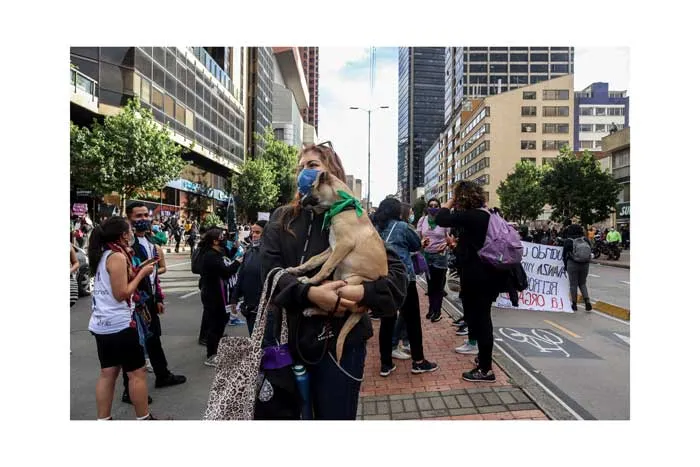 Mujer carga a un perro pequeño entre manifestantes que caminan por una avenida el 8 de marzo de 2021