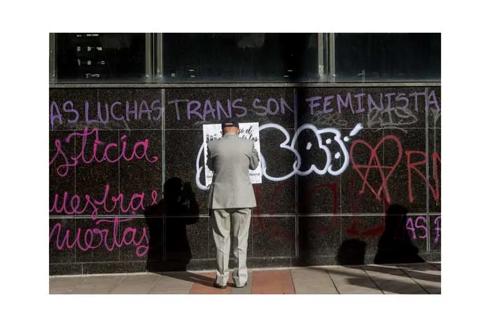 Persona pega un papel en un muro con pintadas como «Las luchas trans son feministas»