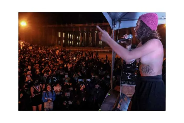 Oradora con gorro rosado habla por micrófono ante una multitud nocturna en la huelga del 8 de marzo de 2021