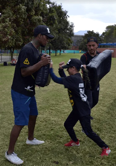 Instructor y niña practican krav magá con escudos de golpeo en un parque