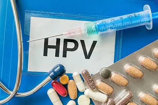 Jeringa, pastillas, estetoscopio y un papel con las siglas «HPV» sobre fondo azul