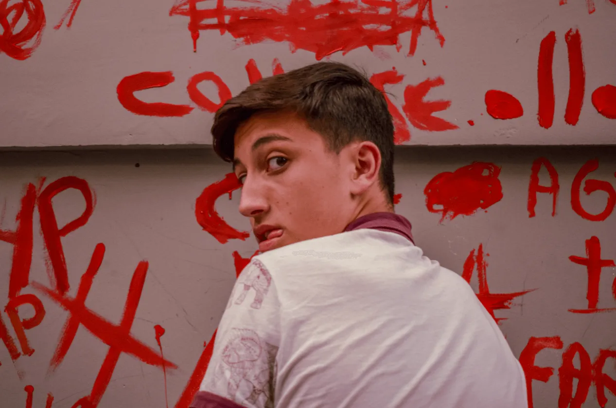 Joven mira sobre su hombro frente a una pared cubierta de pintadas rojas