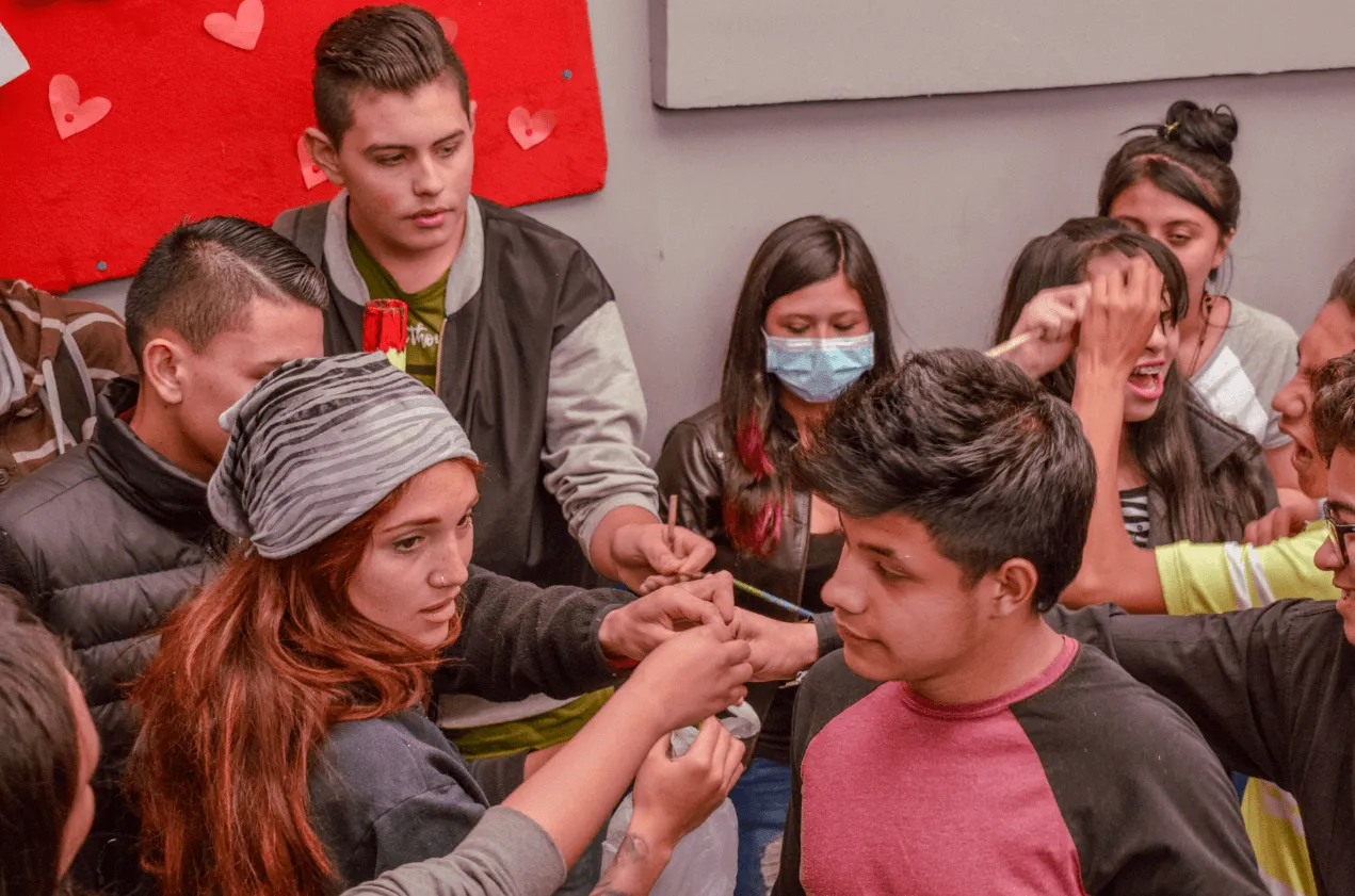 Grupo de jóvenes reunidos en círculo pintando con pinceles durante un taller