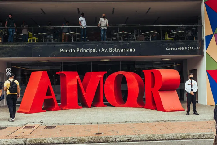 Letras rojas gigantes que forman la palabra «AMOR» frente a un edificio, con personas alrededor
